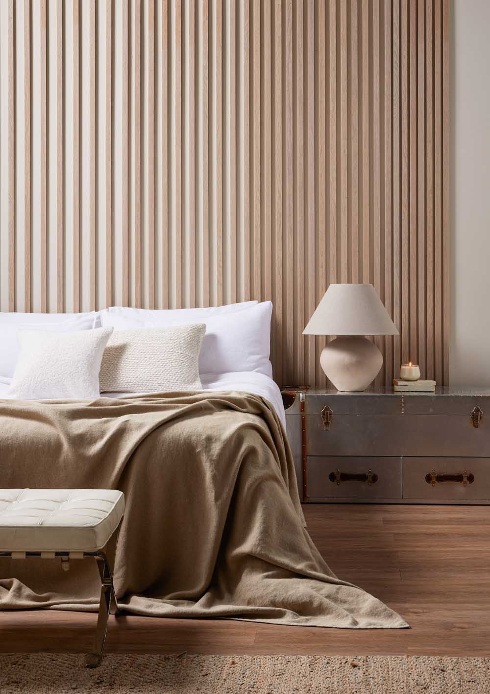 Washed Oak Individual slats on wall behind a bed with cream blanket and white pillows. Slats gradually have smaller gaps between.